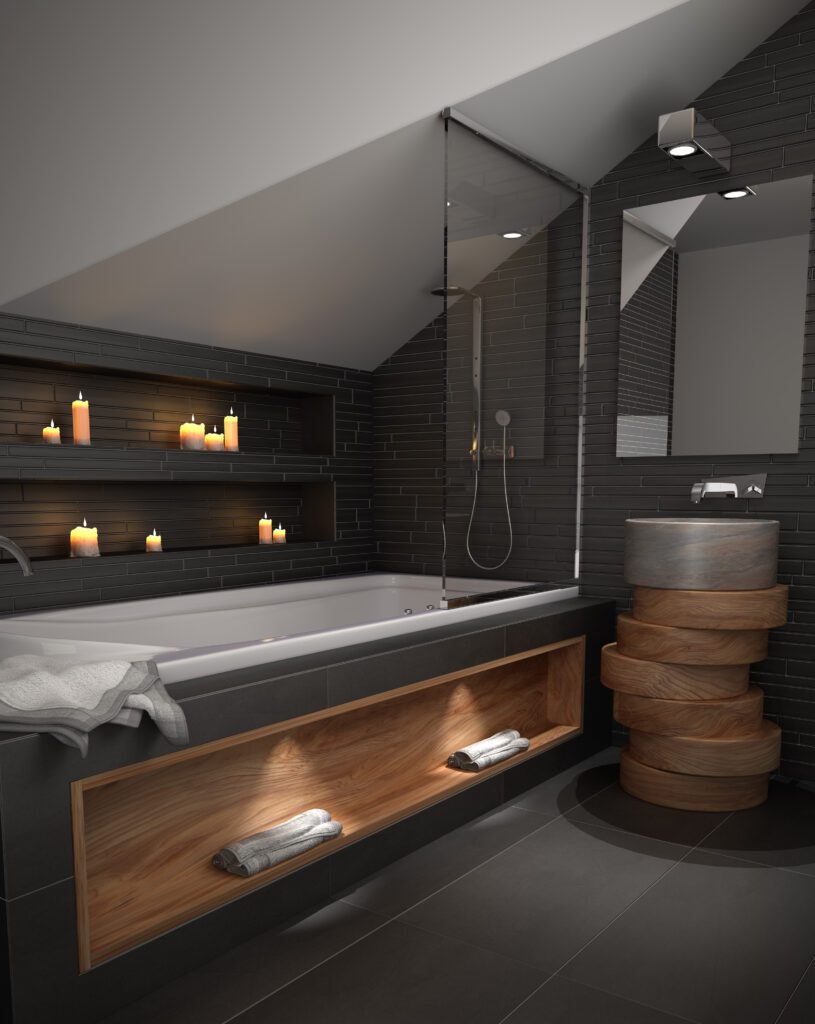 Cuarto de baño moderno con paredes de azulejos negros oscuros y techo inclinado. Incluye una bañera empotrada con un nicho de madera iluminado en la parte inferior para toallas, además de hornacinas integradas en la pared con velas encendidas. A la derecha, un lavabo de piedra cilíndrico sobre una base decorativa de piezas de madera apiladas y un espejo grande con iluminación superior.