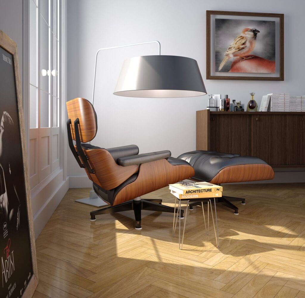 Render 3D de un rincón de lectura contemporáneo en el salón. Combina una butaca tapizada en gris con patas de madera, iluminación auxiliar mediante un flexo de pie negro y una pared de acento con textura de microcemento.